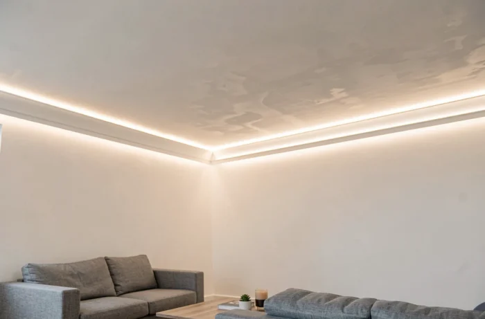 Bandeau LED intégré dans une corniche de plafond diffusant une lumière indirecte douce le long du périmètre d'un salon moderne