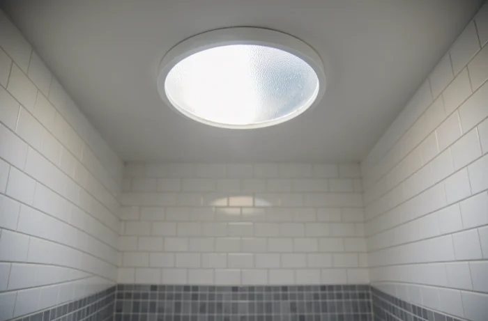 Conduit solaire tubulaire installé au plafond d'une salle de bain aveugle diffusant la lumière naturelle du jour à travers un dôme translucide